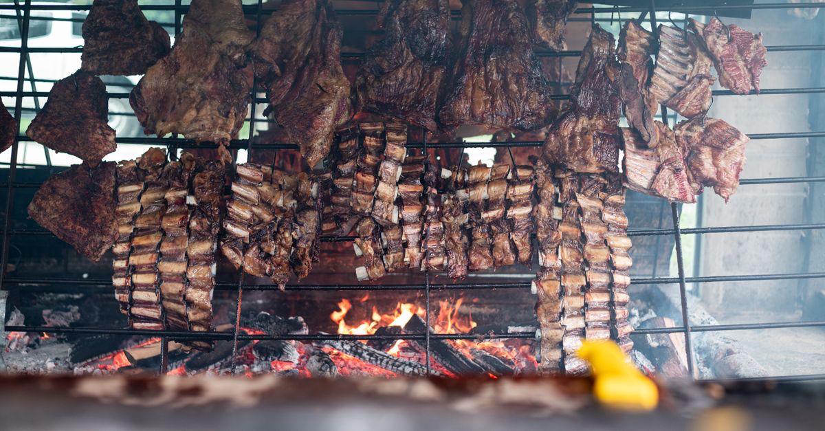 Chorizos y cortes de carne cocinándose sobre una parrilla con brasas